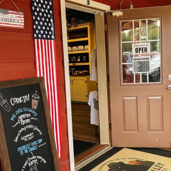 A red building with an open door, an American flag banner, and a chalkboard sign advertising coffee.